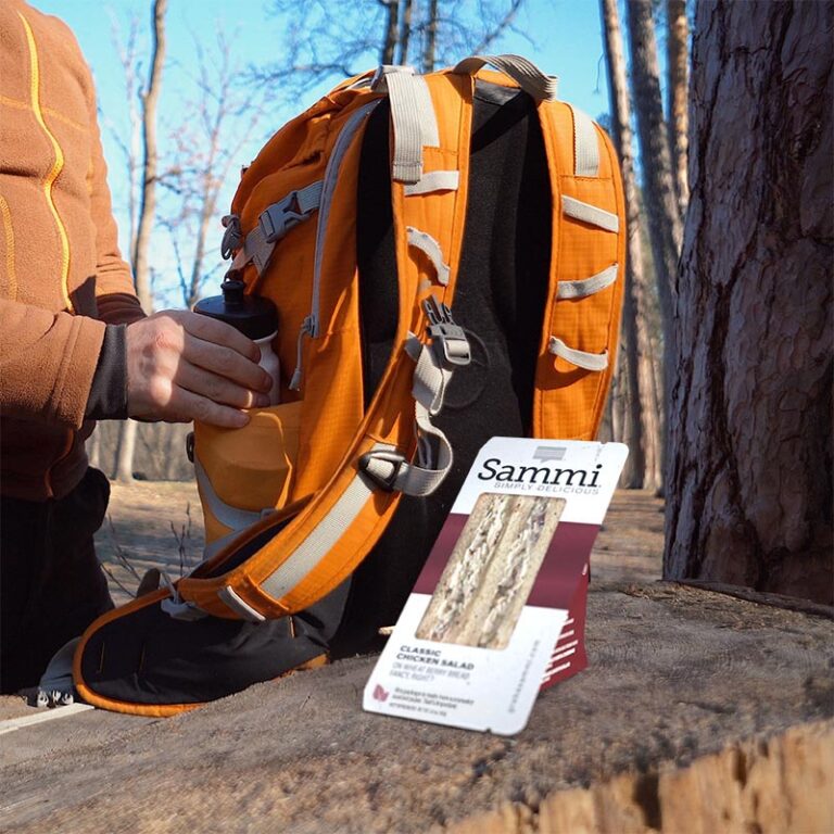 Outdoor image of a man packing a backpack for a hike with a Sammi Classic Chicken Salad Sandwich