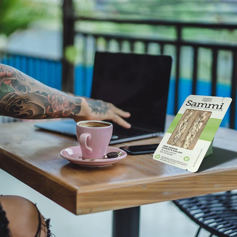 Image of a tattooed young man at an outdoor coffee shop with a Sammi Vegan Chicken Salad Sandwich